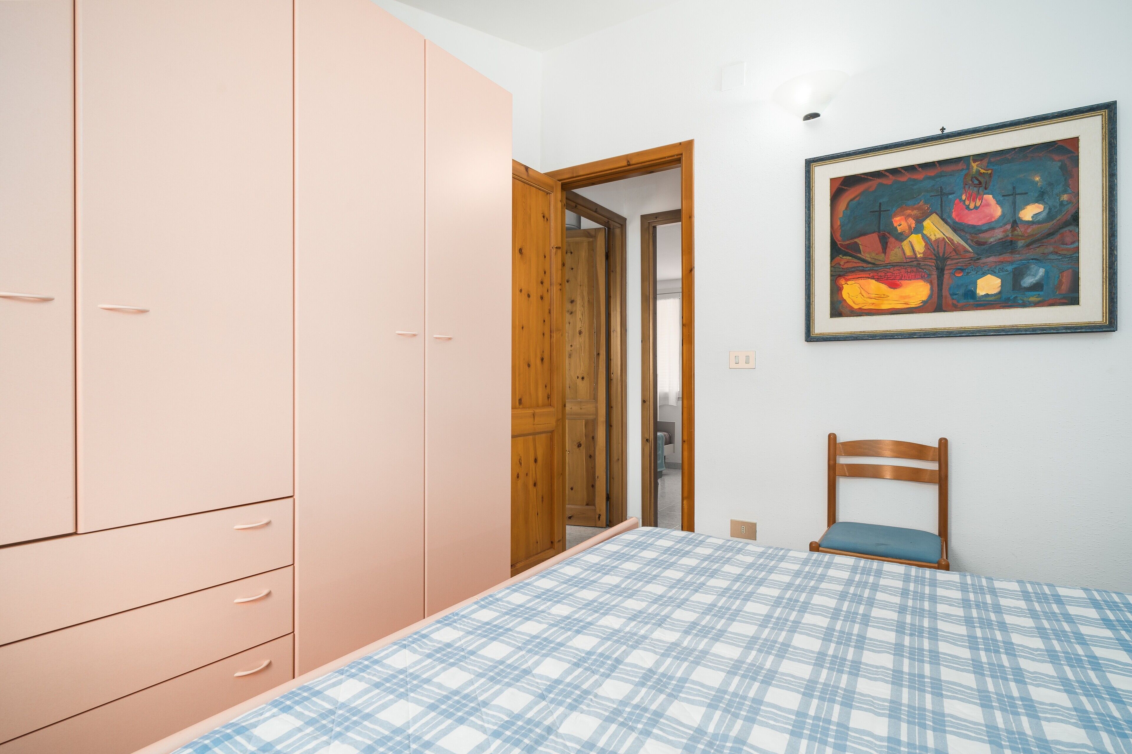 Een slaapkamer met een bed, een kledingkast, een stoel en een schilderij aan de muur.