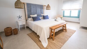 Une chambre à coucher comprenant un lit, des tables de chevet, un banc, une fenêtre avec des stores et une décoration en forme d’étoile de mer.