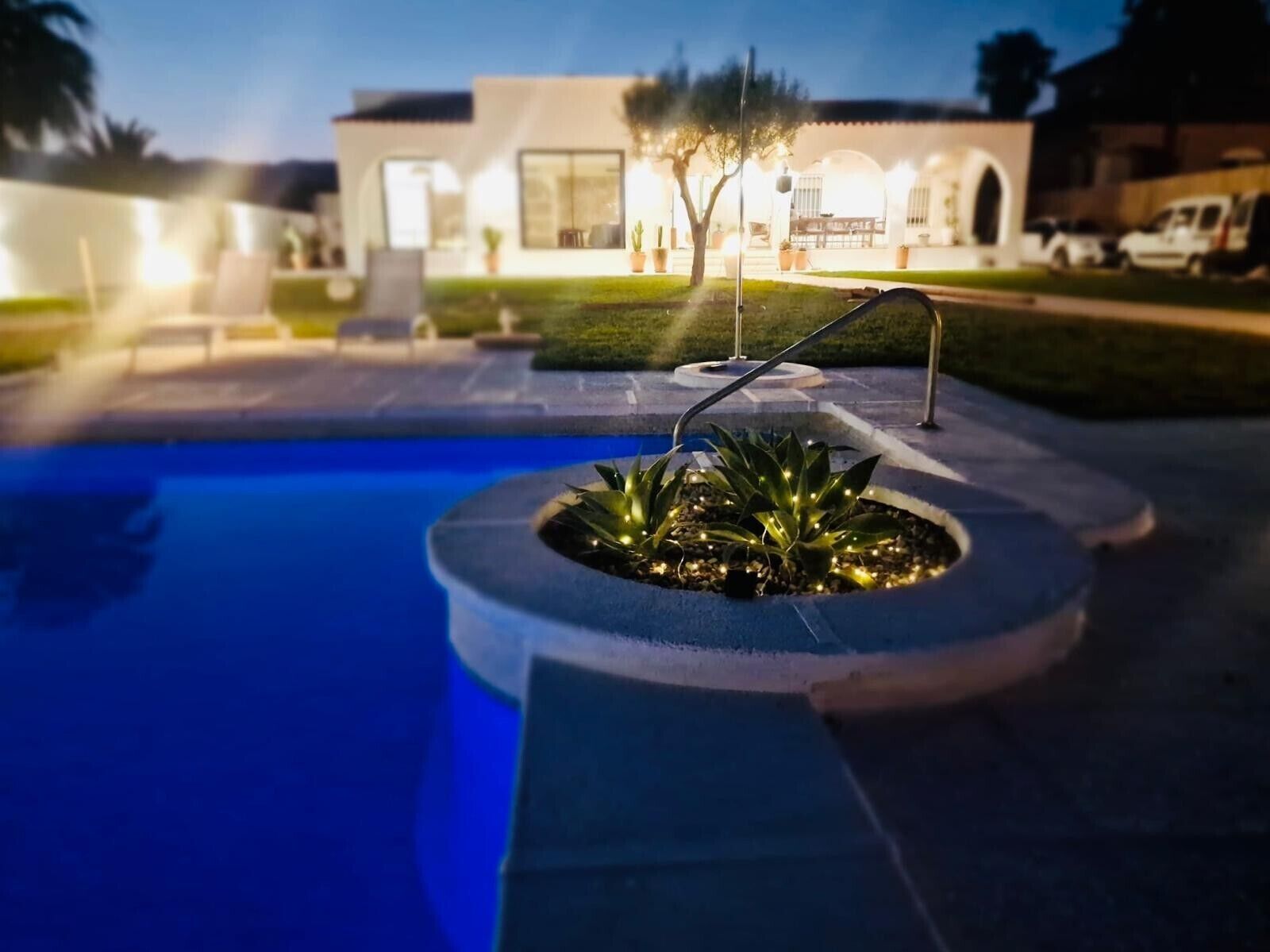 A swimming pool with a circular planter, a white building in the background, and a clear sky.