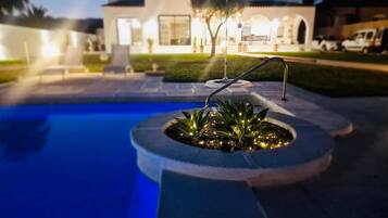 A swimming pool with a circular planter, a white building in the background, and a clear sky.