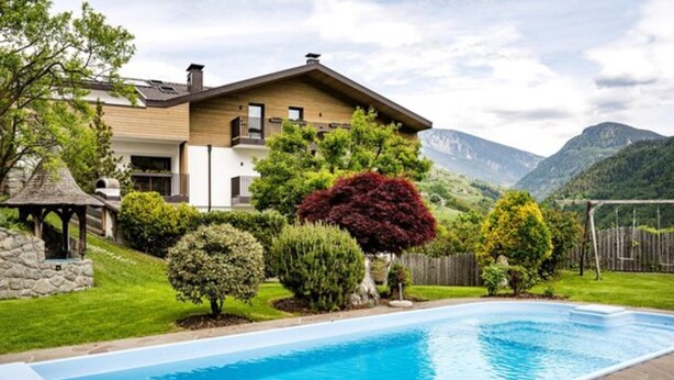 Una casa moderna con piscina, rodeada de jardines cuidados y montañas al fondo.