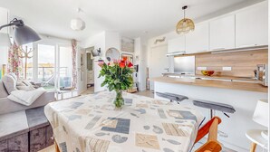 Een moderne keuken met witte kastjes, een houten aanrechtblad en een inbouwoven. Er staat een eettafel met een tafelkleed met dessin en een bloemenvaas.