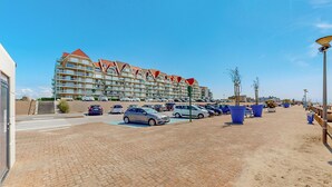 Een parkeerplaats met meerdere auto's, een gebouw met balkons en een heldere lucht.