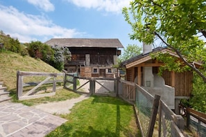 A rustic building with a stone pathway leading to a wooden gate, surrounded by greenery.