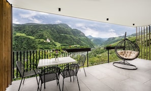 A balcony with a table and chairs, a hanging chair, and a view of a valley with a house.