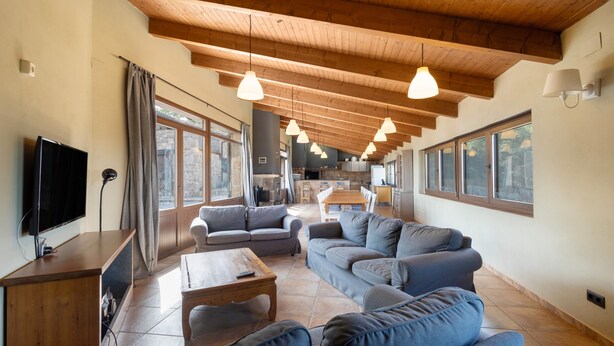 A spacious living area with sofas, a coffee table, a TV, and wooden beams on the ceiling.