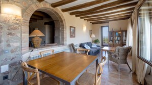 A rustic interior with a stone archway, wooden beams, a dining table with chairs, a sofa, and a bookshelf.
