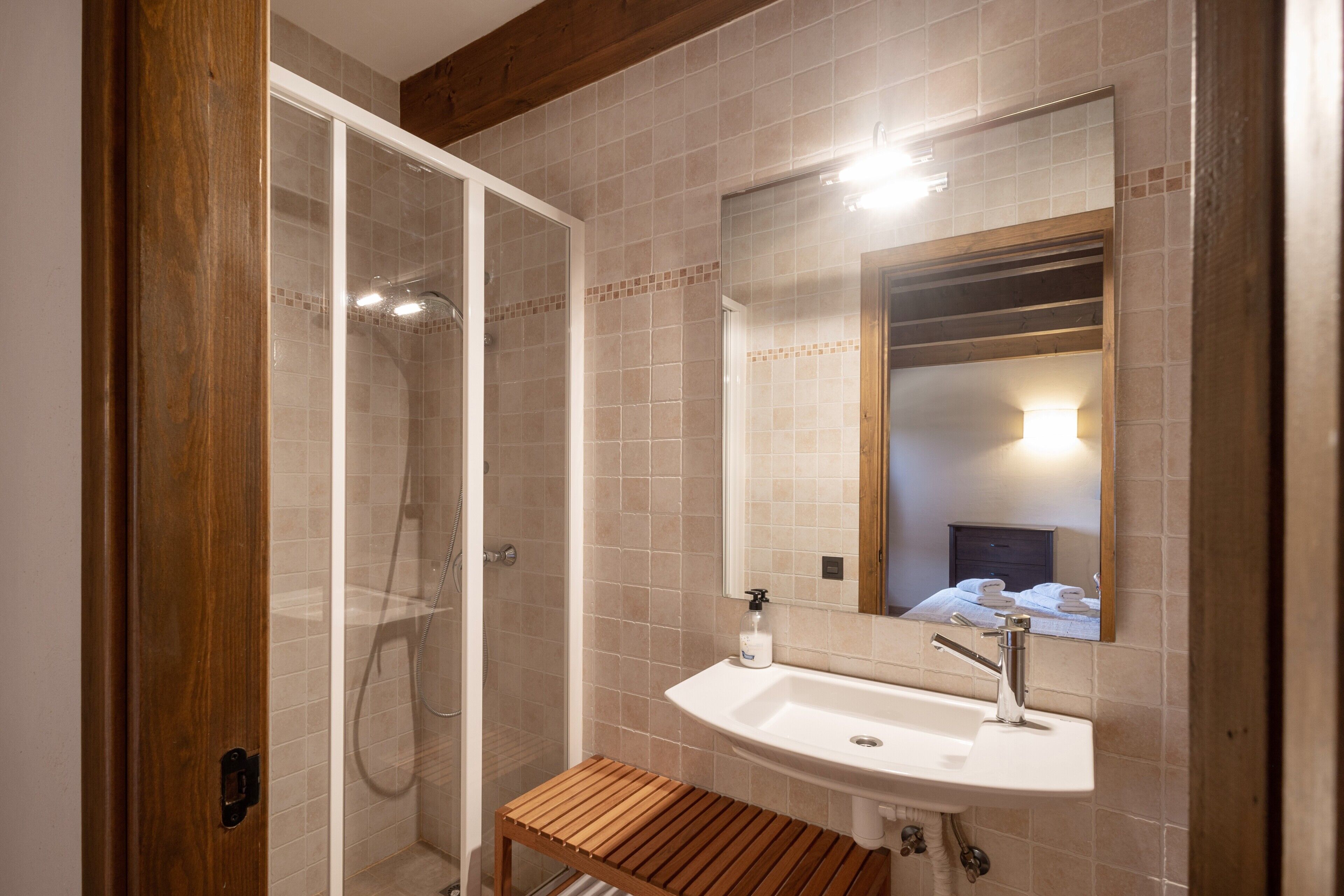 Un baño con ducha, lavamanos y un banco de madera.