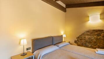 A bedroom with a bed, two bedside tables with lamps, a stone wall, and a wooden ceiling beam.