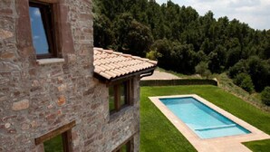 A stone building with a swimming pool, surrounded by a well-maintained lawn and dense forest.