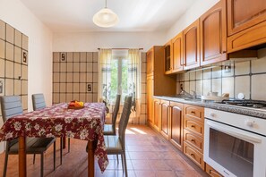 A kitchen with wooden cabinets, a tiled backsplash, a dining table with chairs, and a view through the window.