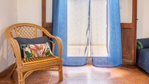 A wicker chair with a floral pillow, a blue curtain, and a wooden door. - Apartment 'Chef House Sorso' with Shared Terrace and Private Garden (Sorso)