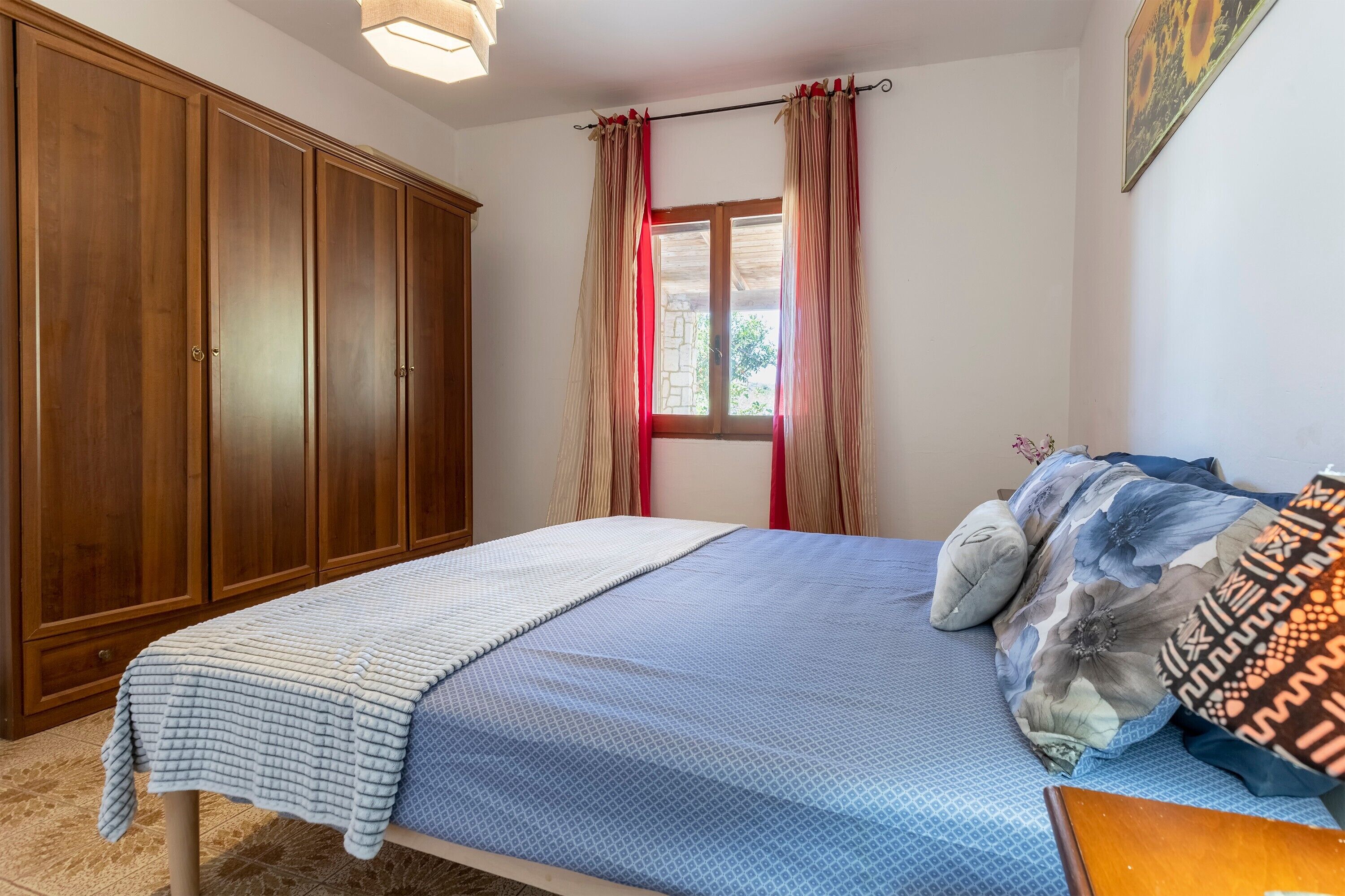 Un dormitorio con cama, un armario, una ventana con cortinas y un cuadro en la pared.
