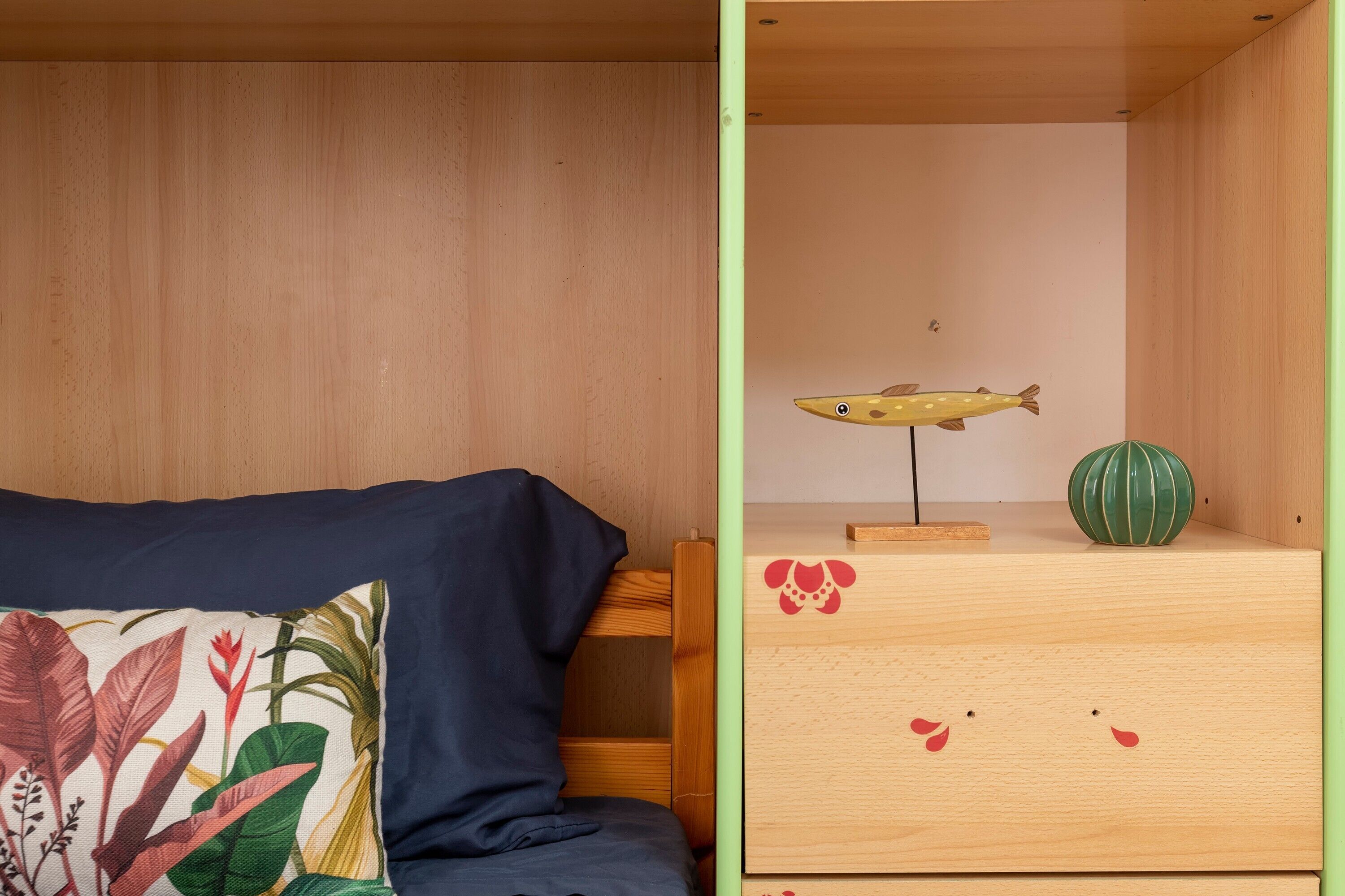 Una stanza con un letto, un cuscino a tema tropicale, un comò in legno decorato con un pesce e un vaso verde.