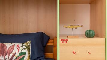 Una stanza con un letto, un cuscino a tema tropicale, un comò in legno decorato con un pesce e un vaso verde.