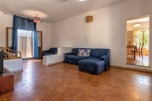 A living room with a blue sofa, a television, and a dining area visible through a doorway.