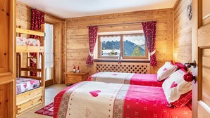 A wooden cabin bedroom with bunk beds, a window with a mountain view, and a bed with heart-patterned bedding.