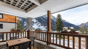 Un balcon avec une table et des chaises en bois, une cheminée en pierre et une vue sur les montagnes.