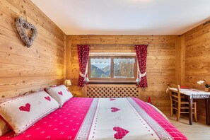 Una habitación de cabaña de madera con una cama, una mesa y un ventanal con cortinas.