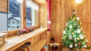 A wooden interior with a Christmas tree, a window with a view of buildings, and a shelf with items.