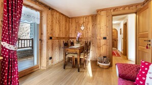 A wooden interior with a dining table, chairs, a red sofa, and a wooden door.