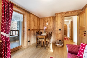 A wooden interior with a dining table, chairs, a red sofa, and a wooden door.