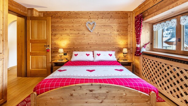 Une pièce en bois avec un lit, une décoration en forme de cœur sur le mur et une fenêtre avec des rideaux.