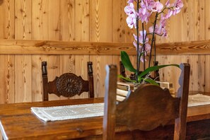 A wooden dining table with a lace tablecloth, a vase with pink orchids, and wooden chairs with carved details.