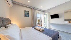 Een hotelkamer met een bed, een flatscreen televisie, een schilderij en uitzicht op de zee door een schuifdeur.
