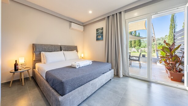 Een moderne hotelkamer met een groot bed, een klein nachtkastje met een fles en glazen, een raam met gordijnen en uitzicht op de omgeving.