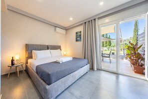 Een moderne hotelkamer met een groot bed, een klein nachtkastje met een fles en glazen, een raam met gordijnen en uitzicht op de omgeving.