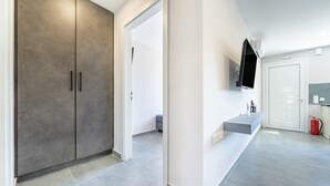 Een moderne hal met een grijze kast, een bevestigde televisie en een rode brandblusser.