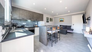 Een moderne keuken met een centraal eiland, een zithoek met een bank en stoelen, en een flatscreen televisie aan de muur.