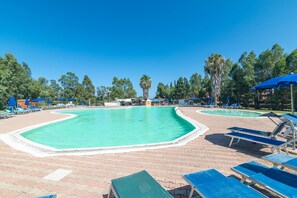 Piscina con sillones de descanso y sombrillas, rodeada de árboles.