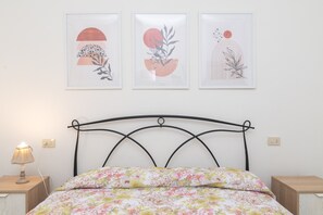 Uma cama com colcha florida, cabeceira de metal e três quadros emoldurados acima.