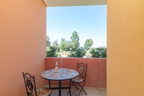 A balcony with a round table and two chairs, a small decorative item on the table, and a view of trees and buildings in the background. - Holiday Home 'Casa Vacanze Olbia' with Shared Pool, Balcony and Air Conditioning (Le Vecchie Saline)