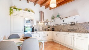 A kitchen with white cabinets, a built-in oven, a stainless steel range hood, and a granite countertop backsplash. - Country House 'Sa Vela' with Private Pool, Wi-Fi and Air Conditioning (Illes Balears)