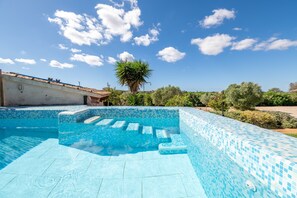 Ein Schwimmbecken mit blauen Mosaikfliesen, einer Palme und blauem Himmel.