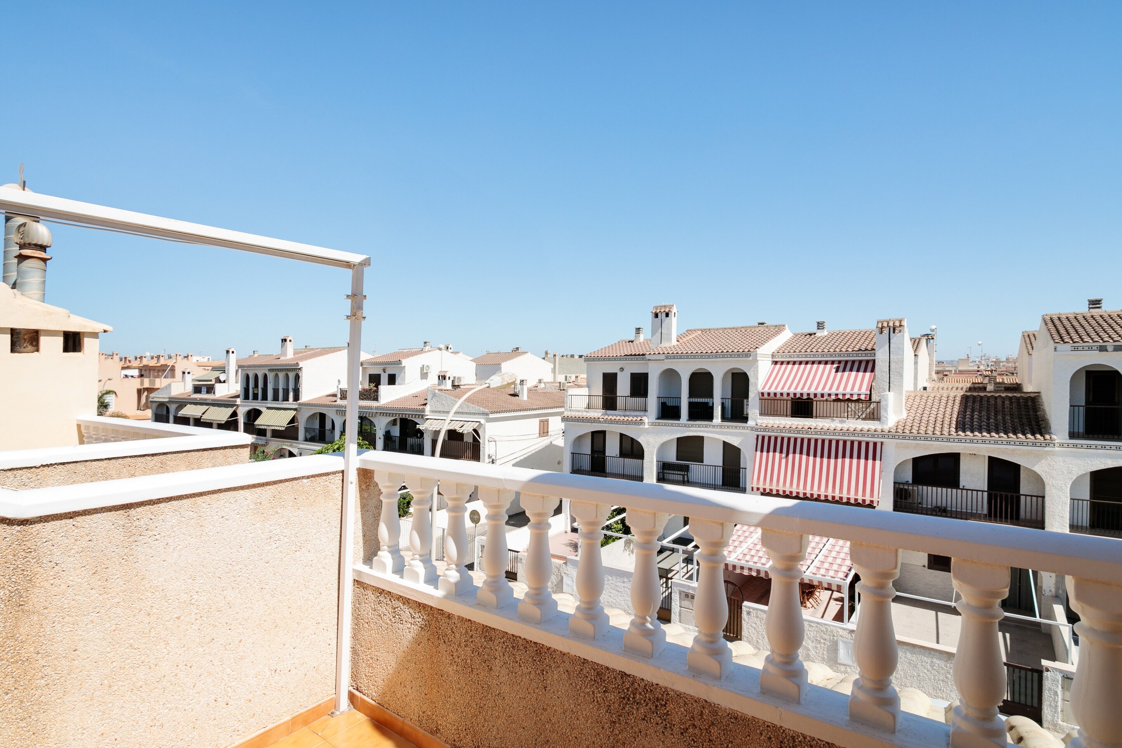 Un balcon doté d’une balustrade blanche donnant sur une cour intérieure bordée de bâtiments traditionnels.