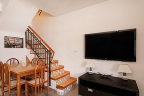 A dining area with a wooden table and chairs, a staircase with patterned steps, a flat-screen TV, and two lamps on a dark console.