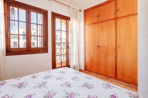 A bedroom with a bed, wooden wardrobe, and a window with a view of buildings.