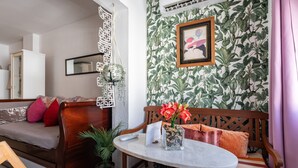 Een kamer met een houten bank, een ronde tafel, een potplant en een muur met een bladerpatroon.
