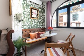 A room with a wooden bench, a round table, and a chair. There is a window with a view of buildings outside. - Apartment 'Benalmadenasol' with Shared Pool, Wi-Fi and Air Conditioning (Benalmádena)