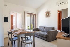 Een moderne woonkamer met een bank, een eettafel met stoelen, een televisie en een decoratief wandkunstwerk.