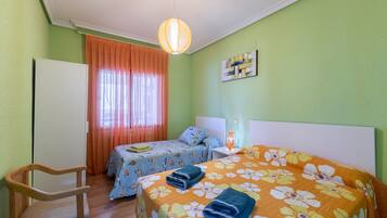 A room with two beds, a chair, a table, and a hanging light fixture.