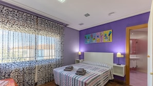 A bedroom with a bed, two bedside tables, a window with curtains, a painting on the wall, and a bathroom visible through an open door. - Casa Rural Kalfonso - 6-Bed Finca in Toledo Province, Private Garden & AC (Mascaraque)