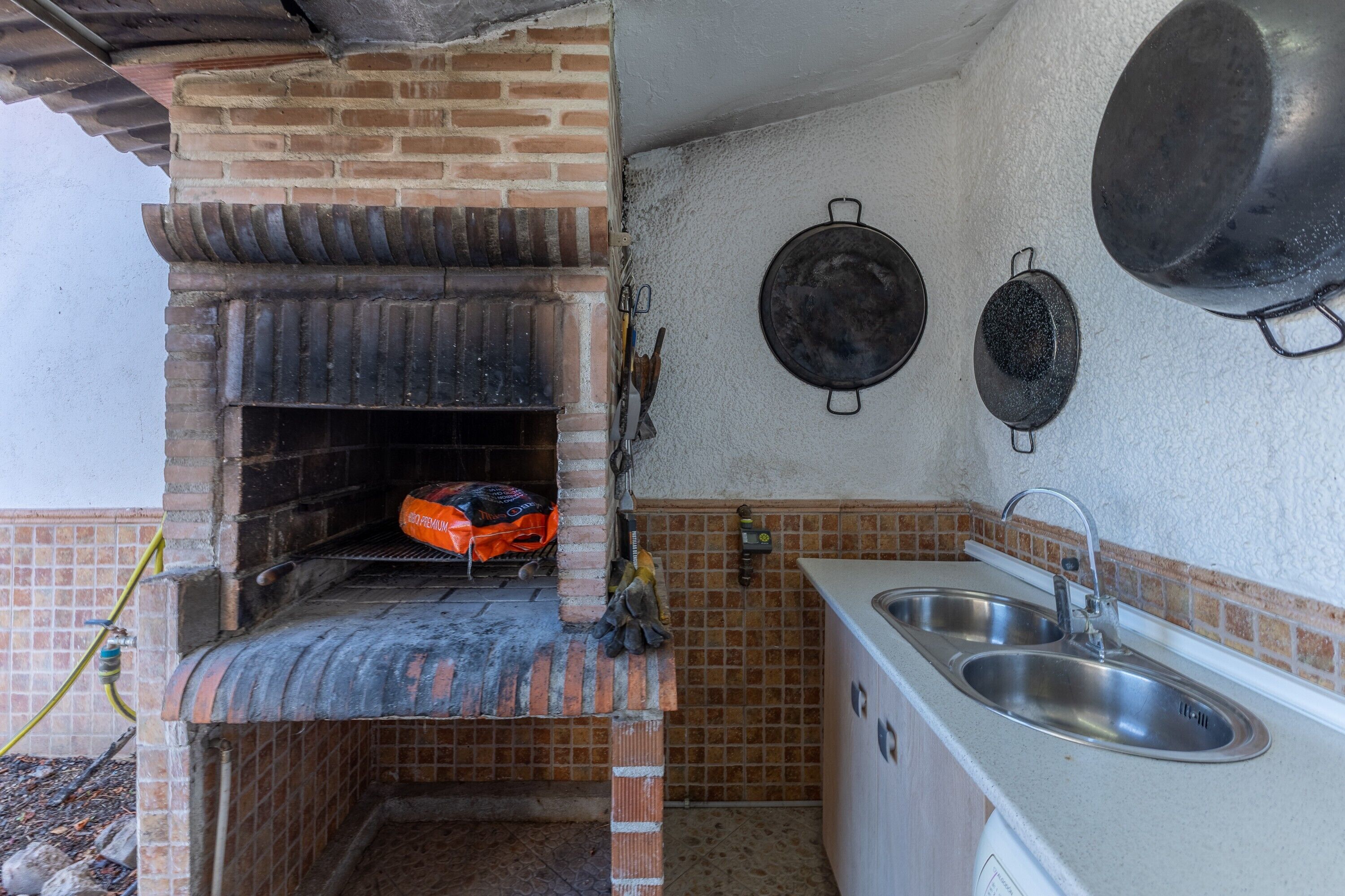 Una cucina con forno a mattoni, lavello e pentole appese.