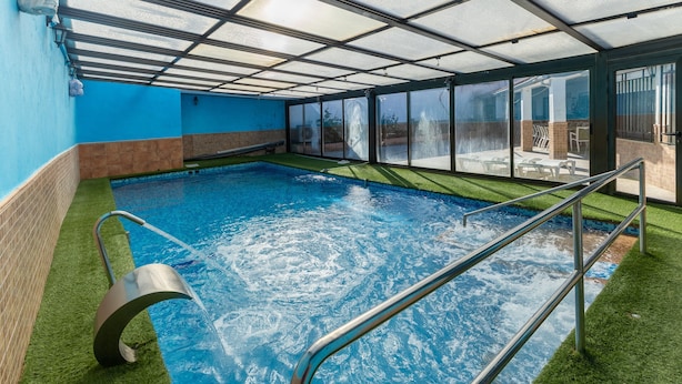 An indoor swimming pool with clear glass walls, a metal ladder, and artificial grass around the pool. - Casa Rural Kalfonso - 6-Bed Finca in Toledo Province, Private Garden & AC (Mascaraque)