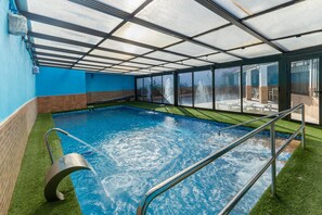 An indoor swimming pool with clear glass walls, a metal ladder, and artificial grass around the pool.