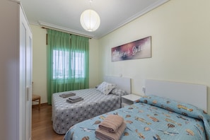 Quarto com duas camas, uma cortina verde, uma obra de arte na parede e uma mesinha de cabeceira.
